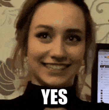 a woman is smiling and holding a cell phone in front of a screen that says yes .