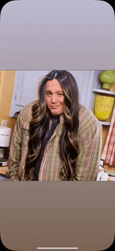 a man with long hair and a plaid shirt is smiling