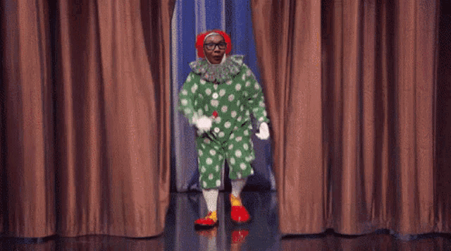 a man in a clown costume is standing in front of a brown curtain .
