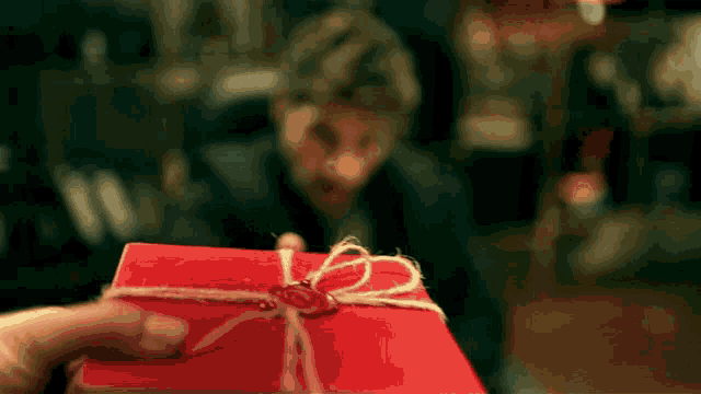 a person is holding a red gift box with a wax seal