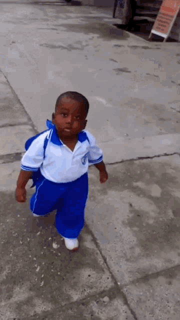 a little boy wearing a white shirt and blue pants is walking down the street