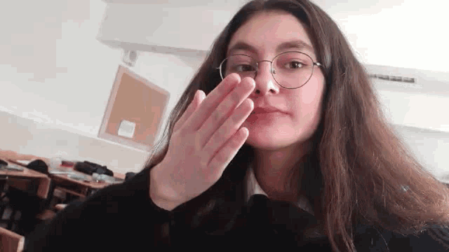 a woman wearing glasses and a black sweater is covering her mouth with her hand .