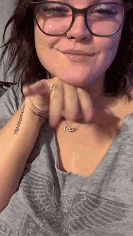 a woman wearing glasses and a necklace has a tattoo on her wrist that reads " i am enough "