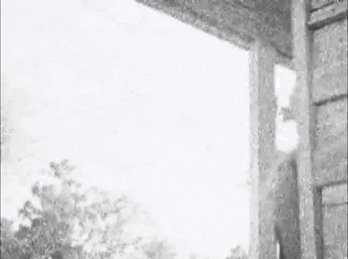 a black and white photo of a woman peeking out of a doorway .