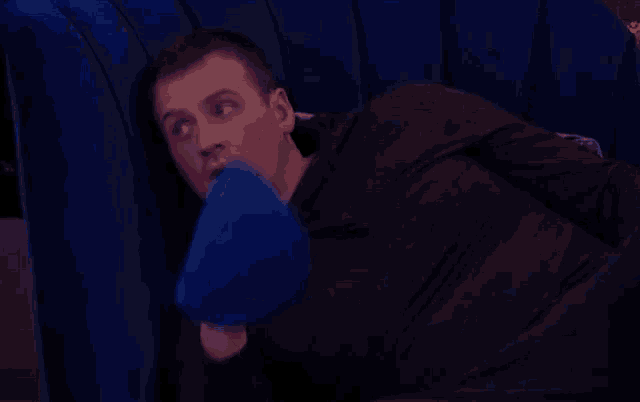 a man is laying on a blue couch with a blue pillow on his face