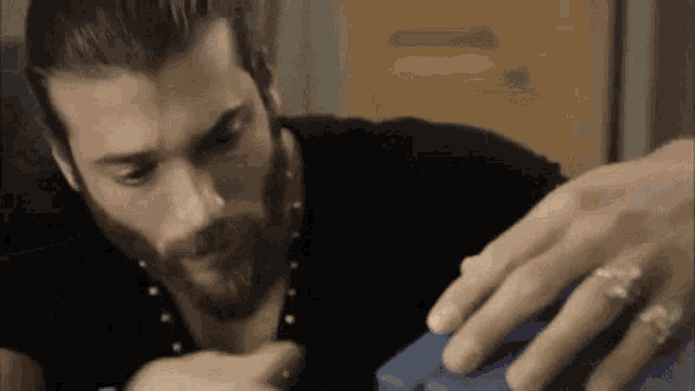 a man with a beard is sitting at a table holding a blue object .
