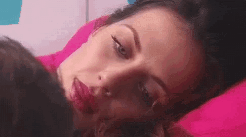 a woman is laying on a pink pillow with her eyes closed and her mouth open .