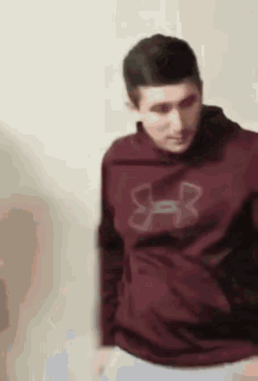 a man in a maroon under armour sweatshirt is standing in front of a wall .