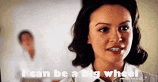 a woman says " i can be a big wheel " in front of a man in a white shirt