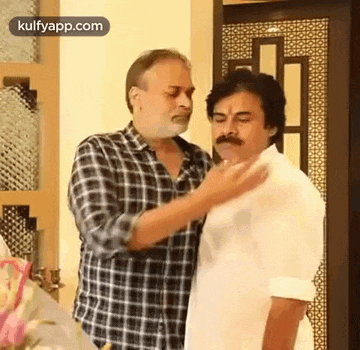 two men are standing next to each other in a room and one of them is touching the other 's neck .
