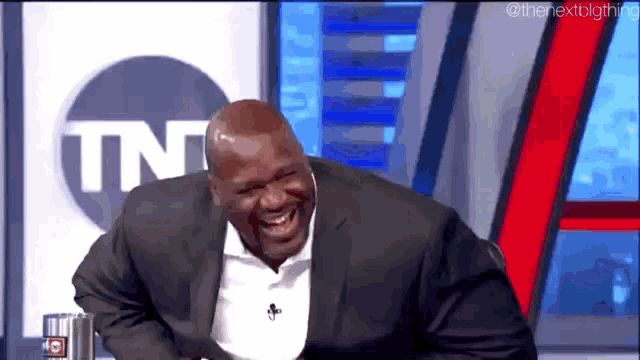 a man in a suit is laughing while sitting in front of a tnt logo .