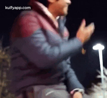 a man is clapping his hands in the dark in front of a light .