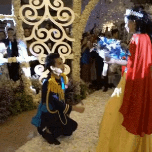 a man is kneeling down in front of a woman in a red dress holding flowers