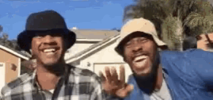two men wearing bucket hats are smiling and waving at the camera .