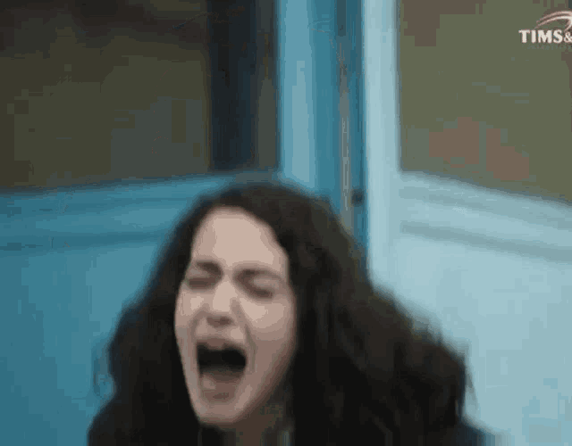 a woman is crying in front of a blue door with tims written on the bottom right