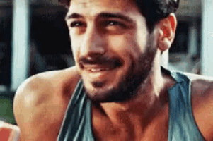 a man with a beard is smiling while wearing a blue tank top .