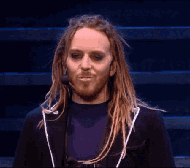 a man with dreadlocks and a beard is wearing a black jacket