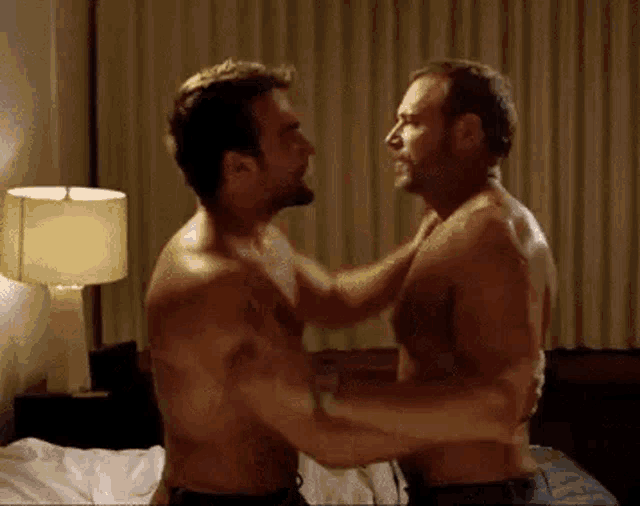 two shirtless men are hugging each other in a bedroom in front of a bed .