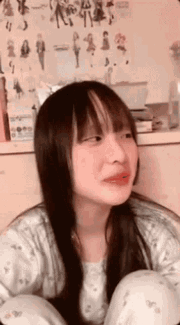 a girl with long hair and bangs is sitting on the floor with her legs crossed .