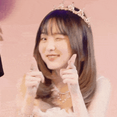 a girl wearing a tiara and a necklace is making a heart with her fingers