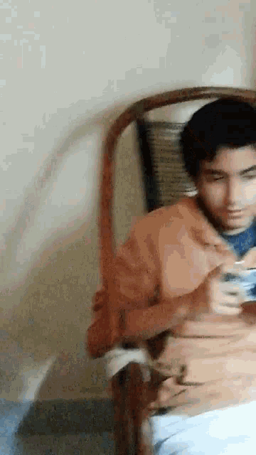 a man in an orange jacket is sitting in a chair holding a cell phone