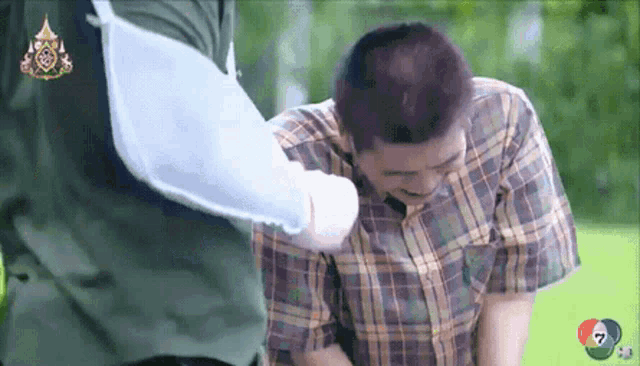 a man in a plaid shirt is being helped by a man in a green shirt