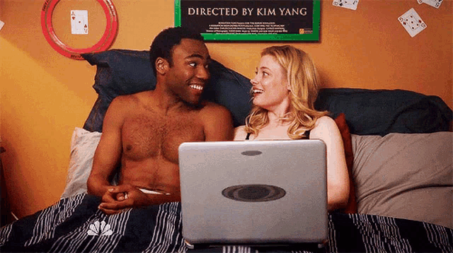 a man and a woman are laying in bed looking at a laptop with a sign that says directed by kim yang
