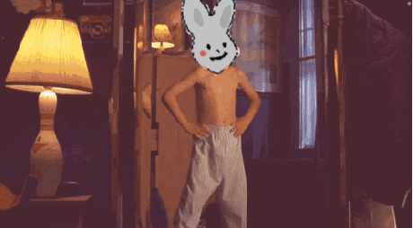 a shirtless boy with a bunny on his head stands in front of a lamp