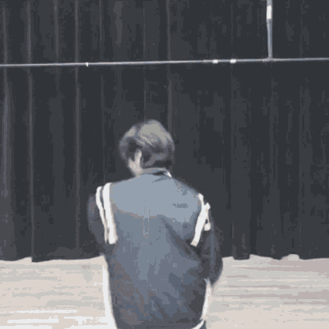 a man in a blue jacket is standing in front of a black curtain .