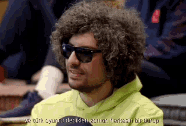 a man with curly hair is wearing sunglasses and a yellow sweatshirt