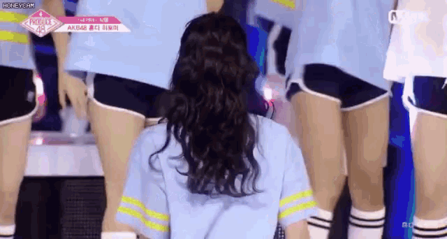 a group of girls are standing on a stage and one of them is wearing a blue shirt and shorts .