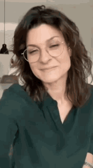 the woman is wearing glasses and a green shirt and smiling .