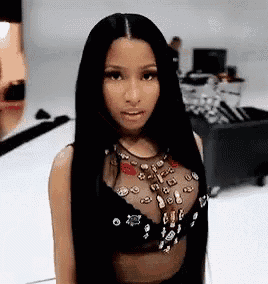 a woman with long black hair is standing in a room wearing a black top and a necklace .