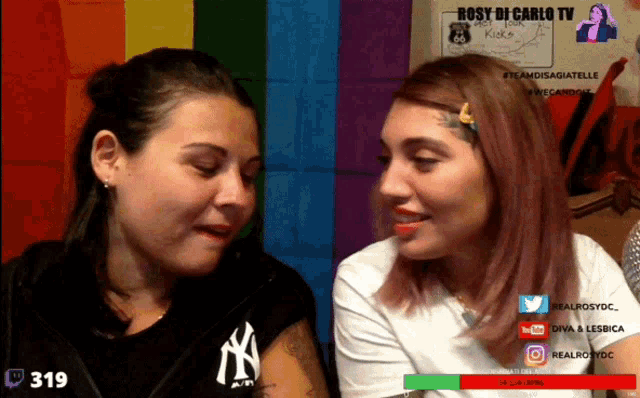 two women are looking at each other in front of a rainbow flag and the number 319 is on the screen