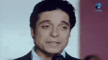 a man in a suit and tie is standing in front of a microphone and making a funny face .