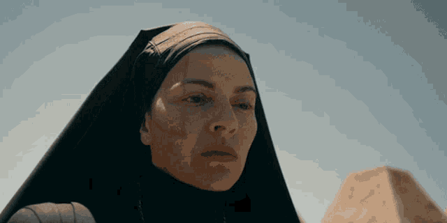 a woman wearing a black veil stands in front of a pyramid in the desert