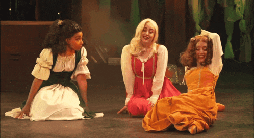 three women are sitting on the floor and one is wearing a red dress