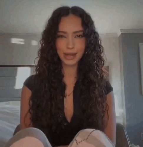 a woman with long curly hair is sitting on a couch in a living room .