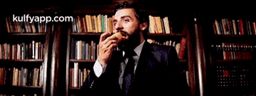 a man in a suit and tie is eating a banana in front of a bookshelf .