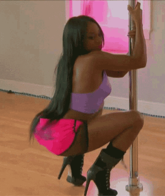 a woman in a purple top and pink shorts is kneeling down on a pole