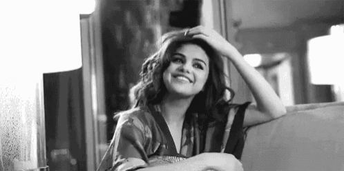 a black and white photo of a woman smiling while sitting on a couch .