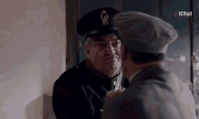 a man in a military uniform talks to another man in a gray hat