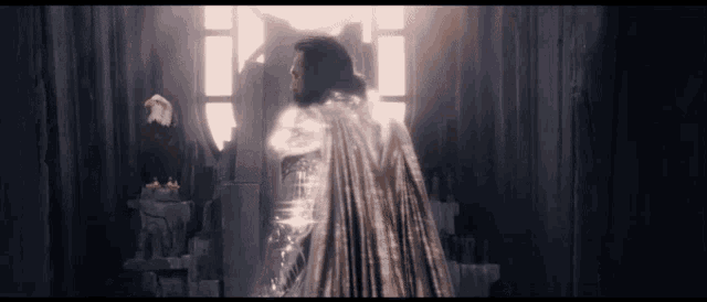 a man in a white cape is standing in front of a window in a dark room .