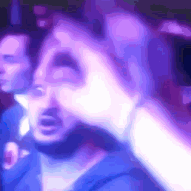 a blurry picture of a man in a blue shirt with purple and white lights behind him