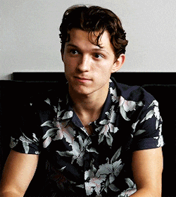 a young man wearing a floral shirt is sitting on a couch looking at the camera .
