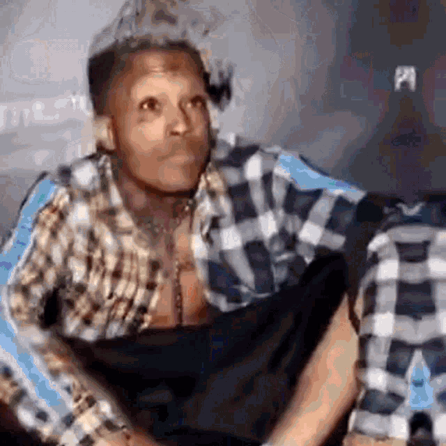 a man in a plaid shirt is sitting on a couch and making a face .