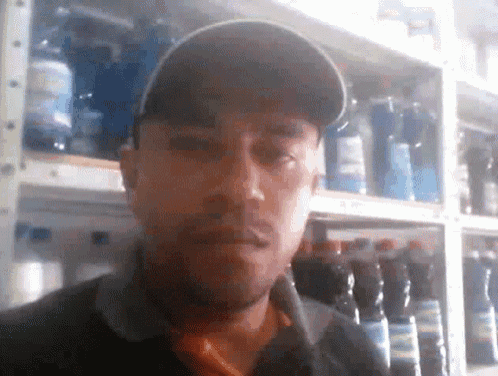 a man in a baseball cap is standing in front of a shelf full of bottles