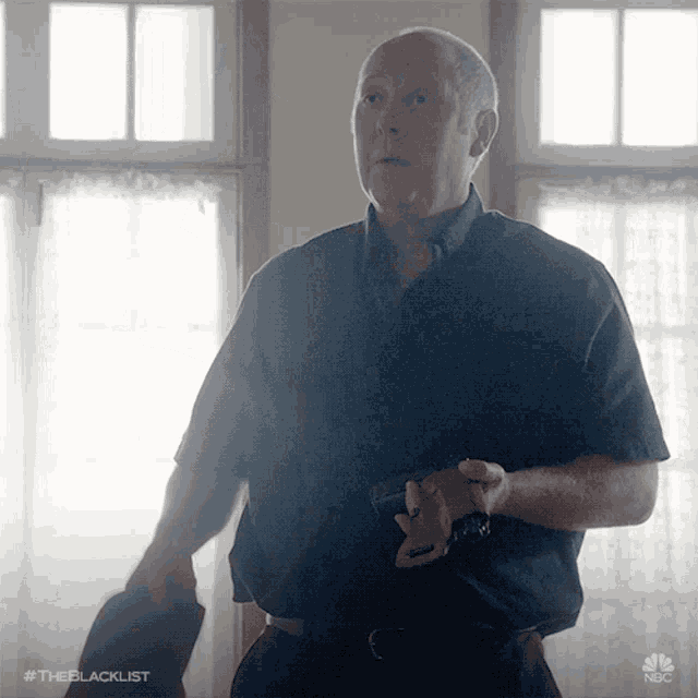 a man in a black shirt is holding a gun in front of a window with the hashtag #theblacklist on the bottom