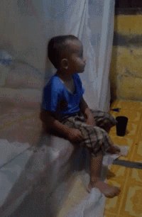 a young boy in a blue shirt squatting on a yellow floor