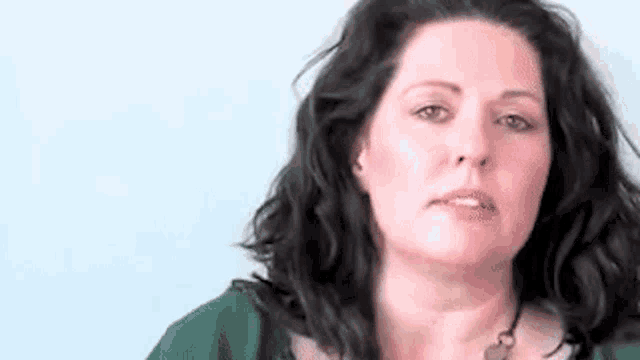 a woman with long black hair is wearing a green shirt and necklace .
